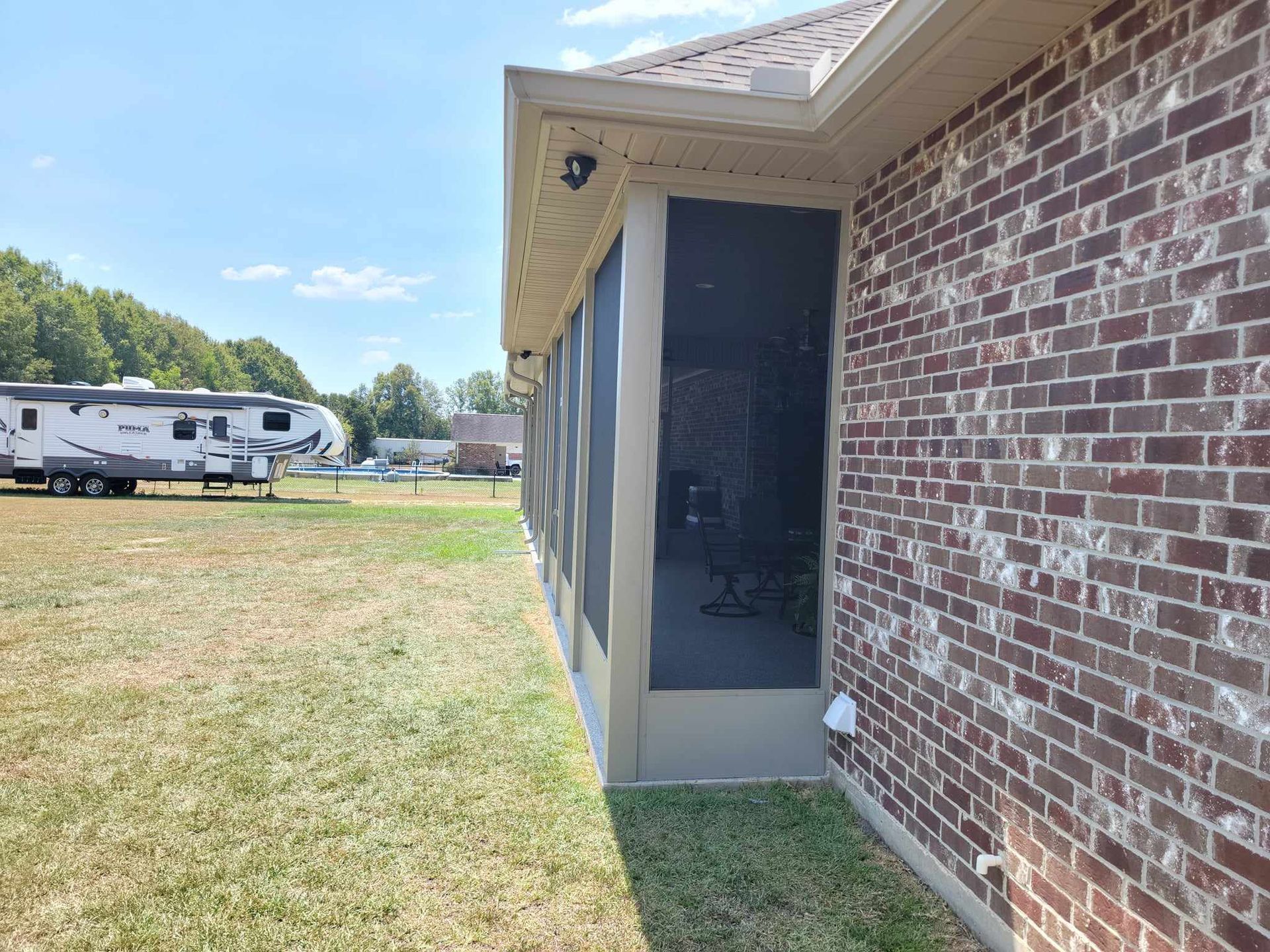 A brick house with a screened in porch and a trailer parked in the background.